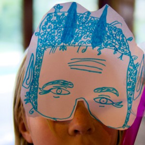 Young girl wears a mask she made with paper and texta
